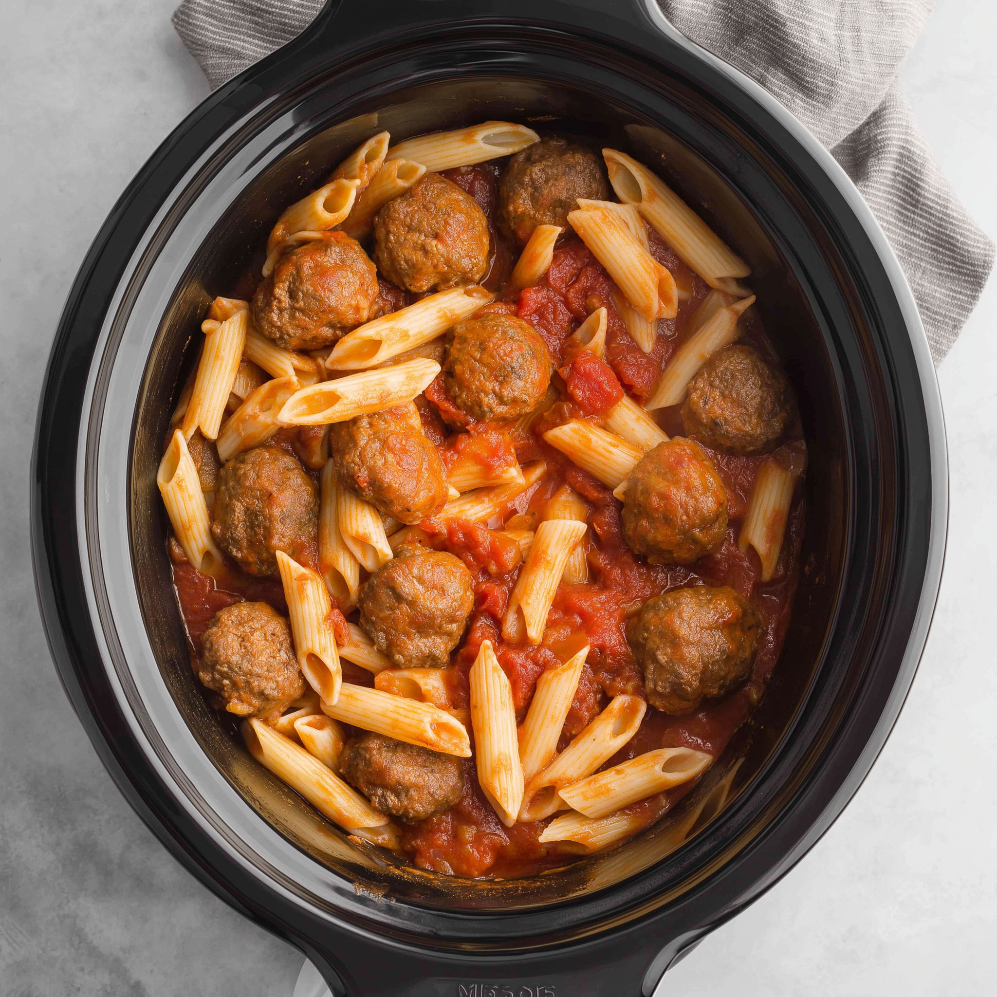 A crockpot filled with pasta and meatballs.